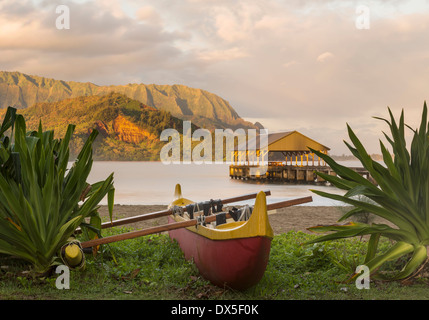 Hawaiian outrigger canoë, avec sur la plage de la jetée de Hanalei, Kauai, Hawaii, USA à l'aube sur les montagnes de Na Pali Banque D'Images