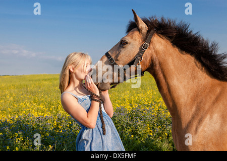 Portrait d'une jeune fille l'embrasser cheval brun dans un champ de colza jaune Banque D'Images