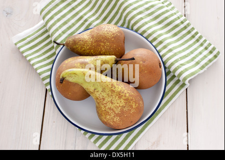 Quatre poires dans un bol blanc sur un fond vert et blanc à rayures serviette cuisine rustique sur un tableau blanc Banque D'Images