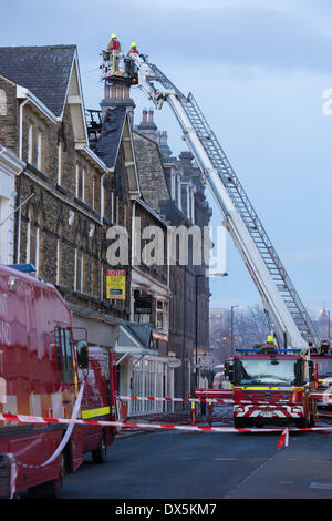 Pompier courageux équipage, à partir de l'échelle (haut moteur) lutter contre le feu avec tuyau d'eau, à l'édifice du centre-ville - Harrogate, North Yorkshire, Angleterre, Royaume-Uni. Banque D'Images