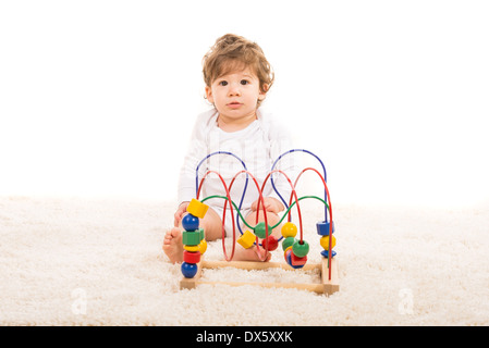 Surpris tout-petit garçon assis sur le tapis de fourrure et de jouer avec des jouets pour fond blanc Banque D'Images