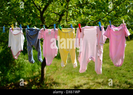 Vêtements de bébé mignon petit accroché sur le fil a linge au soleil dans un jardin de printemps vert. Banque D'Images