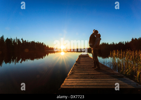 Un jeune couple baiser debout sur un quai alors que les couchers de soleil sur le lac Beaver. Banque D'Images