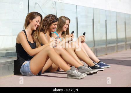 Groupe d'adolescent girls smiling happy messages sur le téléphone intelligent assis sur le plancher à l'extérieur Banque D'Images