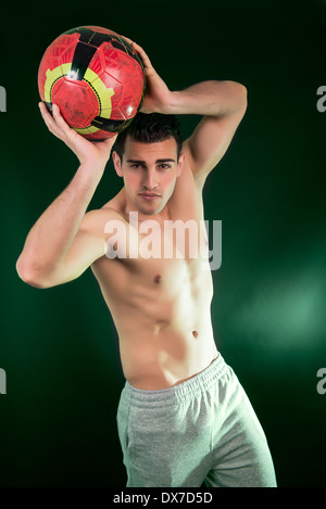 Jeune homme musclé avec ballon sur fond vert Banque D'Images