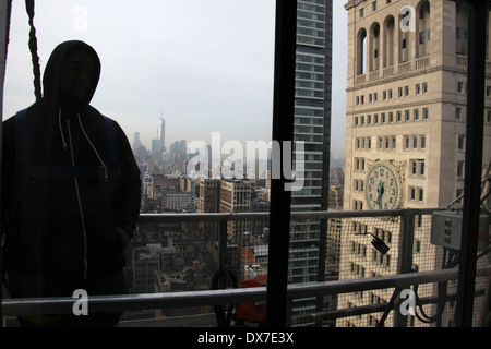 Vue intérieure d'une rondelle de fenêtre en silhouette portant un sweat en se tenant debout sur des échafaudages dans un gratte-ciel de la ville de New York Banque D'Images