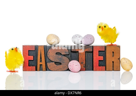 Le mot Easter en vieux bois typo avec un jouet poussins et oeufs en chocolat bonbons couverts, isolé sur un fond blanc. Banque D'Images