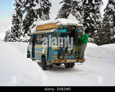 L'Inde, au Cachemire, Gulmarg, les passagers se tenant à l'extérieur de l'autobus sur la route couverte de neige à Tangmarg Banque D'Images