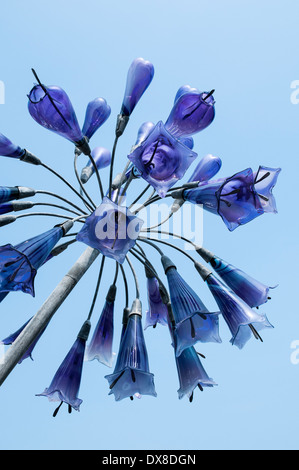 Une 'fleur' sculpture en verre suspendue sur un poteau de métal, vu du dessous isolés contre un ciel bleu clair. Banque D'Images