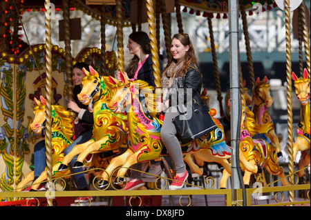 Trois jeunes femmes équitation chevaux de bois de couleur vive sur un merry go round, Londres, Angleterre, Royaume-Uni. Banque D'Images