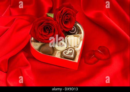 Roses rouges et de délicieux pralinés chocolat en forme de coeur d'or sur fond de soie boîte cadeau Banque D'Images