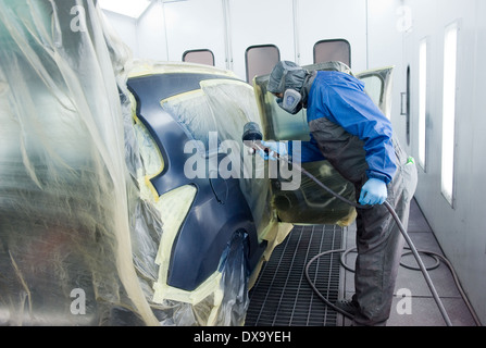 Une voiture qui est peintre professionnel peinture le travail du corps d'une voiture dans une boîte de peinture d'un garage avec un aérographe. Banque D'Images