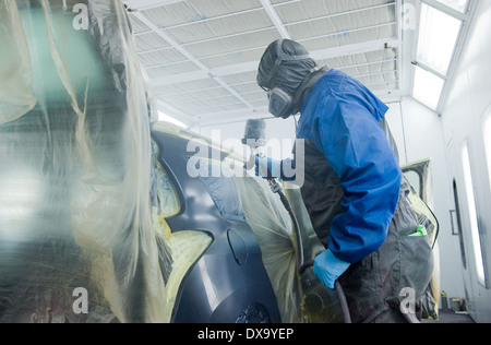 Une voiture qui est peintre professionnel peinture le travail du corps d'une voiture dans une boîte de peinture d'un garage avec un aérographe. Banque D'Images