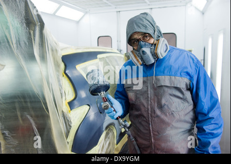 Une voiture qui est peintre professionnel peinture le travail du corps d'une voiture dans une boîte de peinture d'un garage avec un aérographe. Banque D'Images