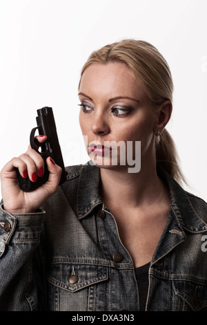 Blond woman holding handgun et à la recherche autour, portant veste en jean. Banque D'Images