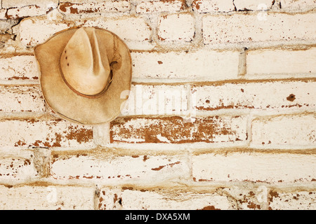 Une paille cowboy hat accroché sur un mur en brique adobe qui était blanc, avec un espace libre pour le texte à droite de la hat. Banque D'Images
