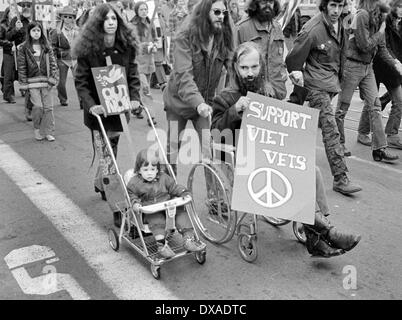 Le contraste entre un enfant trop jeune pour marcher et manifestant contre la guerre en fauteuil roulant poussé à San Francisco, Californie en 1972 Banque D'Images