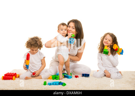 Heureux maman et les enfants jouant avec des blocs de construction maison et assis ensemble sur un tapis Banque D'Images