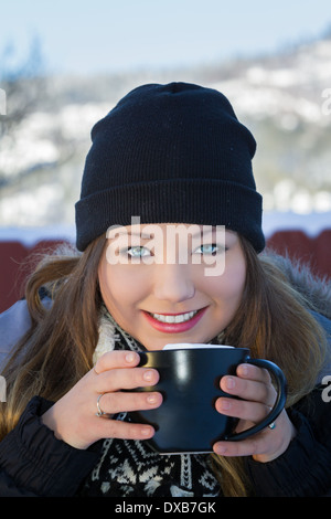 Jolie jeune femme avec de beaux yeux bleus de boire du chocolat chaud à l'extérieur dans des conditions d'hiver enneigé Banque D'Images