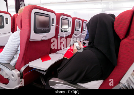 Femme arabe musulmane dans une burqa en utilisant son téléphone portable sur un avion de Virgin Atlantic de Dubaï à Londres UK Banque D'Images