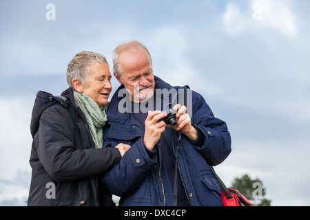 Couple de personnes âgées en tenant un autoportrait sur un appareil photo numérique compact qui pose à l'air libre et le soleil avec leurs têtes rapprochées souriant à l'objectif Banque D'Images