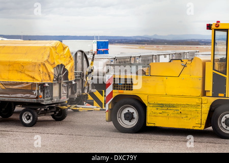 Chariots chargés de bagages dans un aéroport debout sur le tarmac sous bâches jaunes attendent d'être chargés à bord d'un avion Banque D'Images