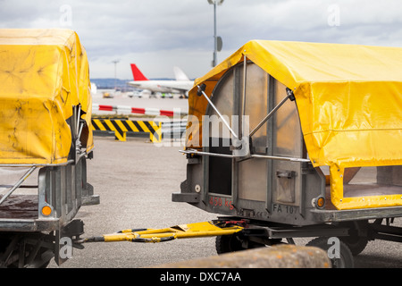 Chariots chargés de bagages dans un aéroport debout sur le tarmac sous bâches jaunes attendent d'être chargés à bord d'un avion Banque D'Images