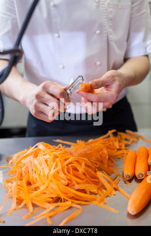Chef en uniforme préparation des bâtons de carotte le tranchage à la main comme il se tient à un comptoir de cuisine, vue en gros plan de ses mains Banque D'Images