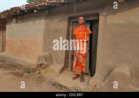 Femme en sari rouge debout devant sa maison de terre entrée. tribu santhal, Hardhekitand village, Jharkhand, India Banque D'Images