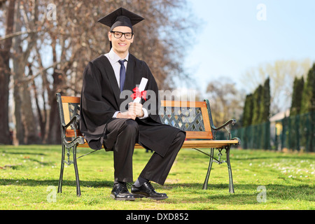 Male student posing avec diplôme assis sur un banc dans le parc Banque D'Images