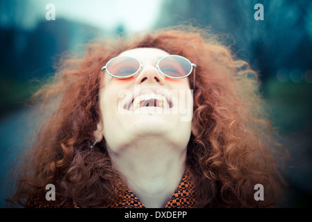 Belle jeune femme avec des cheveux bouclés rouge Sunglasses at the park Banque D'Images