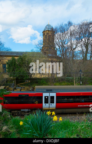Un train à la gare de Saltaire passe en face de Saltaire United Reformed Church, Saltaire, Bradford, Yorkshire, Angleterre. Banque D'Images