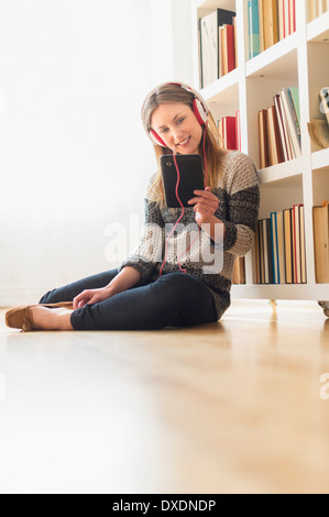 Jeune femme assise sur le plancher et à l'écoute de musique sur tablette numérique Banque D'Images