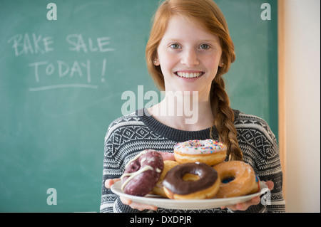 Portrait of Girl (12-13) holding plaque avec donut Banque D'Images