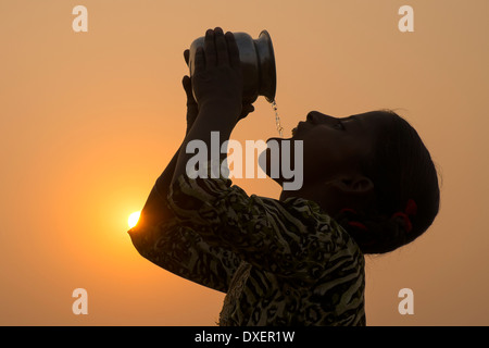 L'Inde, l'Uttar Pradesh, Agra,silhouette de fille de l'eau potable verseuse au coucher du soleil. Banque D'Images