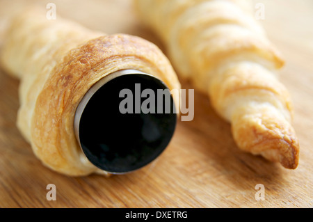 Faire la crème faite maison avec des cornes de pâte feuilletée, enroulé autour de la crème de moules métalliques de l'avertisseur sonore. Banque D'Images