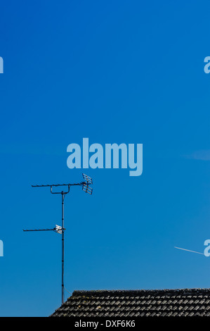 Old style TV par antenne / l'antenne sur le dessus de toit de tuiles noires principalement contre ciel bleu. Banque D'Images