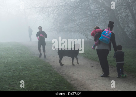 Un jogger passe devant une famille alors qu'ils prendre leur chien de compagnie pour une promenade dans un épais brouillard dans l'Essex. Banque D'Images