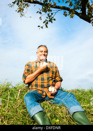 Portrait of farmer sitting in field eating apple, Allemagne Banque D'Images