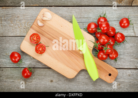 Les tomates cerise avec un couteau sur une planche à découper sur fond de table en bois Banque D'Images