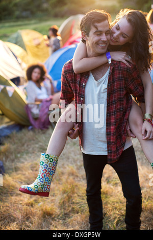 Man piggybacking woman outside tents at music festival Banque D'Images