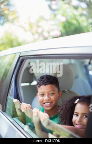 Portrait of happy brother and sister leaning out car window Banque D'Images