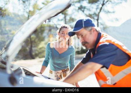 Femme regardant roadside mechanic vérifier moteur de voiture Banque D'Images