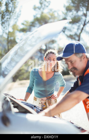 Femme regardant roadside mechanic vérifier moteur de voiture Banque D'Images