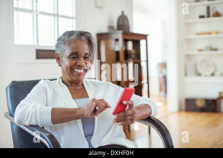 Happy senior woman text messaging with cell phone in living room Banque D'Images
