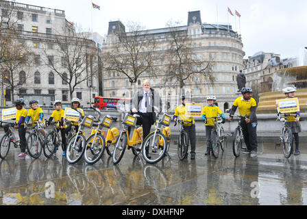 Trafalgar Square, Londres, Royaume-Uni. 26 mars 2014. Le maire de Londres Boris Johnson s'assoit sur l'un des 100 vélos spéciaux placés autour de Londres pour marquer qu'il y a 100 jours pour le départ du Tour de France, il est rejoint par un groupe d'enfants tous vêtus de maillots jaune. Crédit : Matthieu Chattle/Alamy Live News Banque D'Images