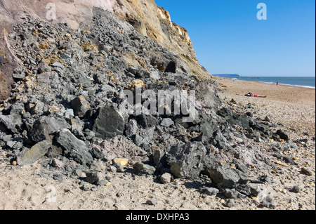 Baigneurs sur la plage dangereusement près de la chute de roches de l'érosion des falaises à Hengistbury Head, Dorset, UK Banque D'Images