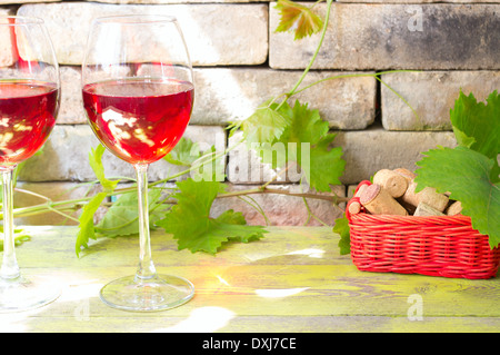 Deux verres de vin rouge contre un mur de briques et de vignobles. Près de panier avec wine corks. Banque D'Images