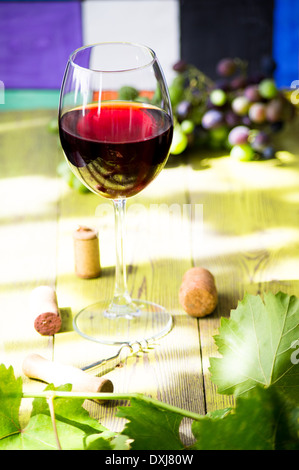 Verre de vin rouge sur une table en bois avec des feuilles de vigne, de tire-bouchon et wine corks et un groupe de jeunes les raisins. Banque D'Images
