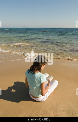 Young woman sitting on beach reading book vue arrière Banque D'Images